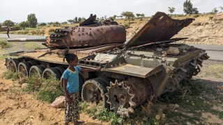 A child standing next to a tank which has been left abandoned and rusting. 