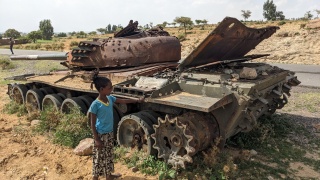 A child standing next to a tank which has been left abandoned and rusting.