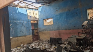Image of a classroom which has been left ruined after recent conflict. The roof appears to have caved in with debris covering the floor. 