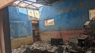 Image of a classroom which has been left ruined after recent conflict. The roof appears to have caved in with debris covering the floor.