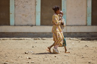 Two girls walking across a dry and dusty school courtyard.