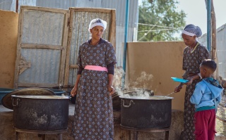 Volunteers serving school meals to a child waiting.