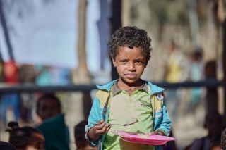 Image of a child eating from a plate looking at the camera.