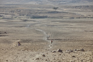 Image showing a dry and barren landscape with figures walking in the distance.